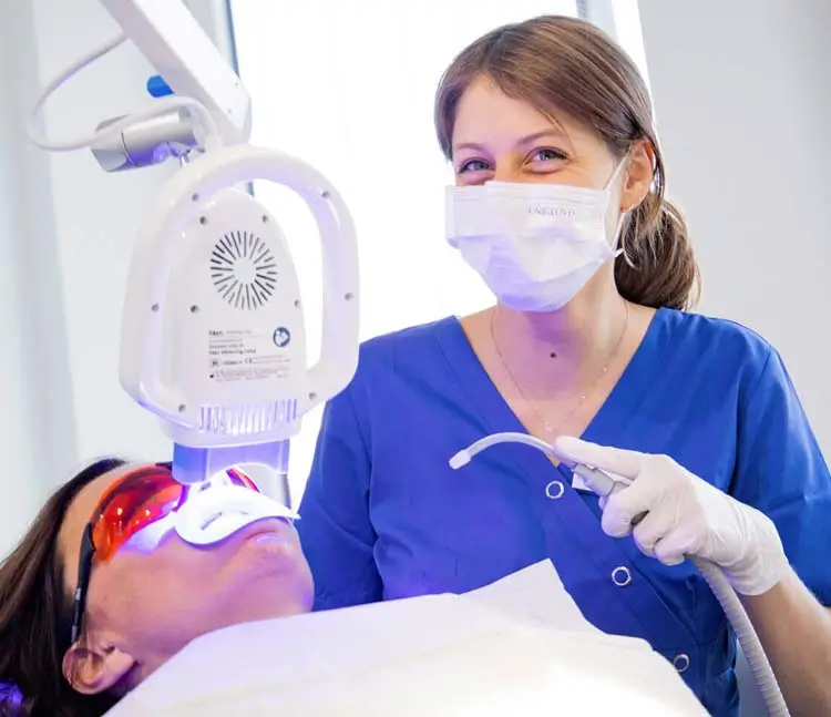 Prophylaxeassistentin sitzt mit einem Sauger neben der Patientin am Behandlungsstuhl